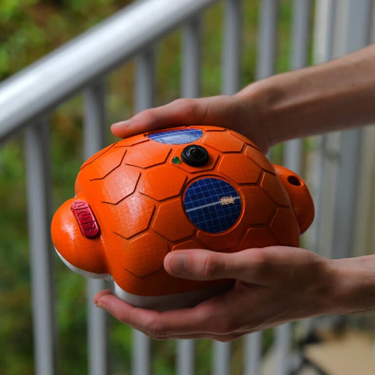 Real-world photograph of the Guardian Pool Alarm, held with two hands against a blurred balcony background.