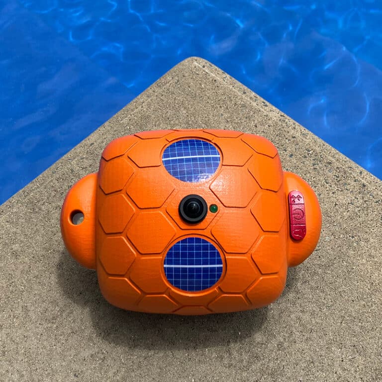 Top-down real-world photograph of the Guardian Pool Alarm sitting on a ledge near a pool with water visible.