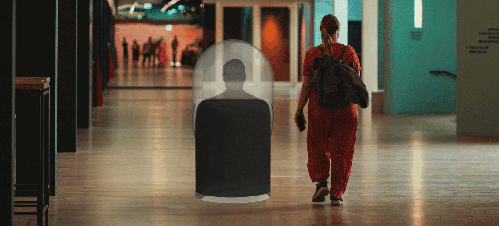 Woman and CADAH robot in a lobby, walking away from the camera.